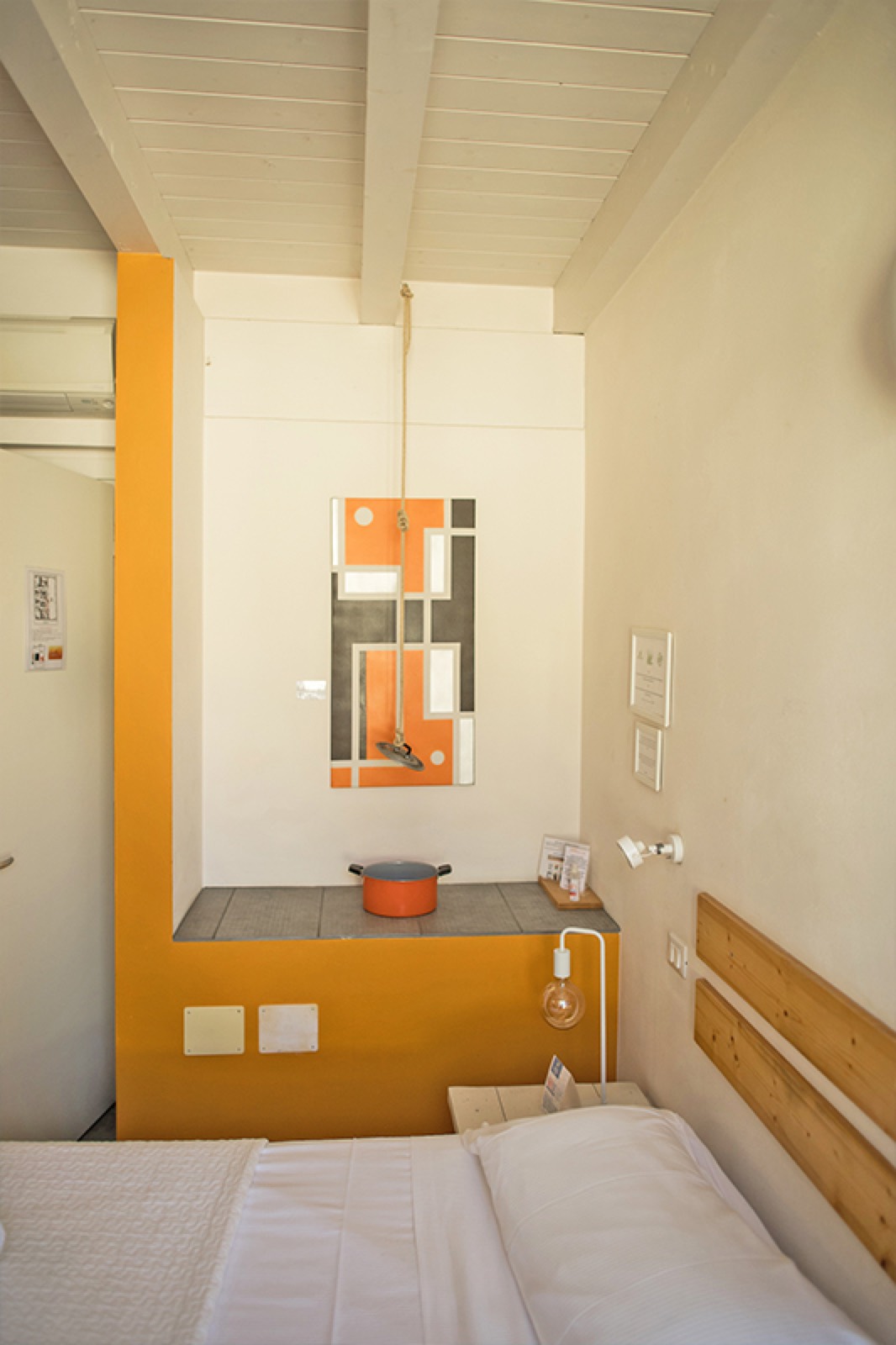 La Camera Mandarino: colonna e nicchia color arancio, opera d'arte geometrica, travi bianche a vista e letto con testiera in legno