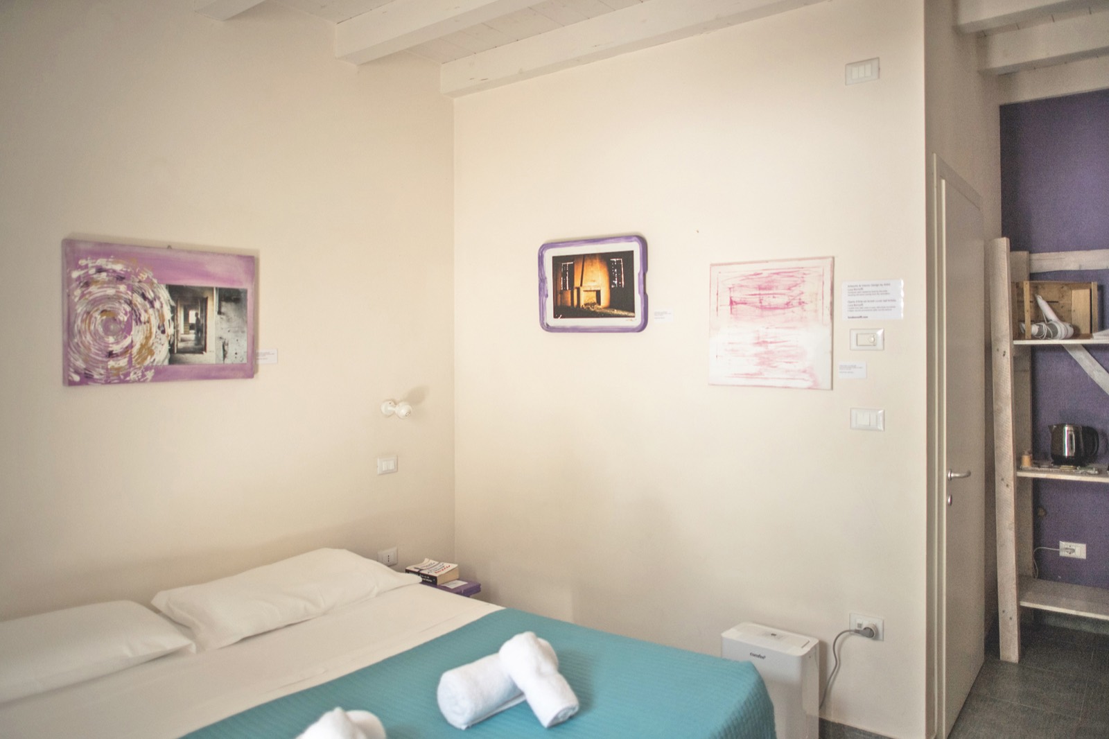 La Camera Melanzana: letto con copriletto verde acqua, opere d'arte dalle cornici viola melanzana, nicchia color melanzana e travi bianche a vista