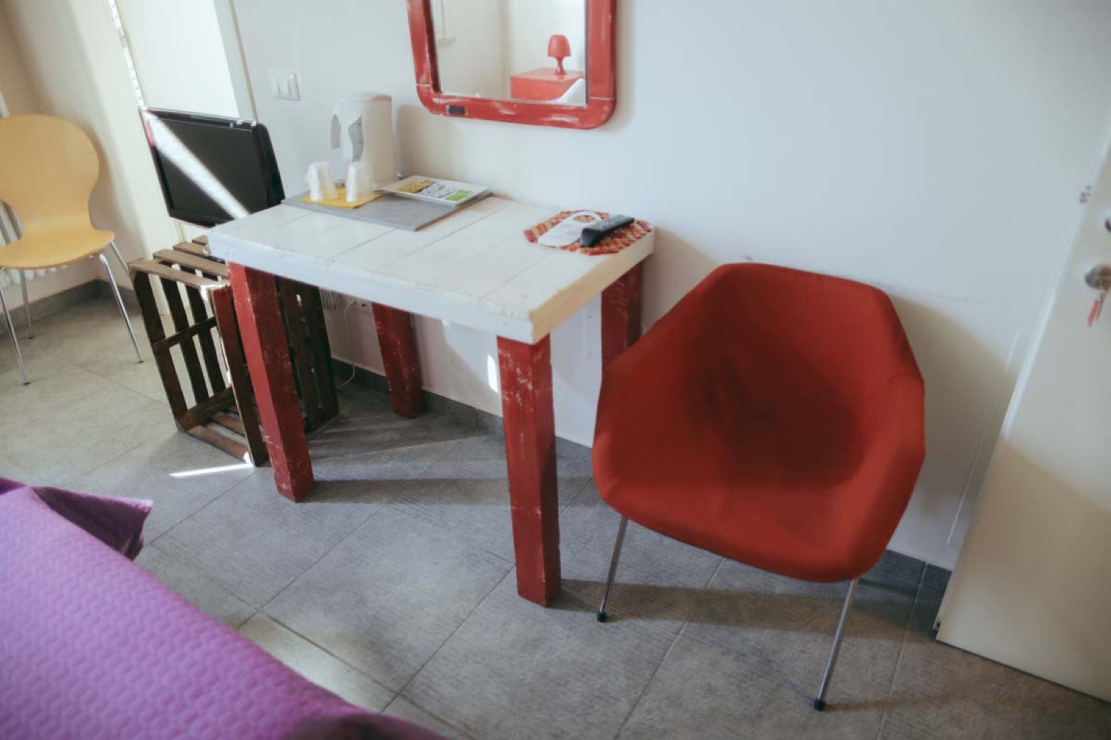 La Camera Pomodoro: scrittoio in legno di recupero dipinto di rosso, poltroncina di design rossa e specchio dalla cornice rossa su pareti bianche