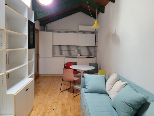 Il monolocale mansardato a Bologna: cucina, tavolo e divano sotto il tetto in legno